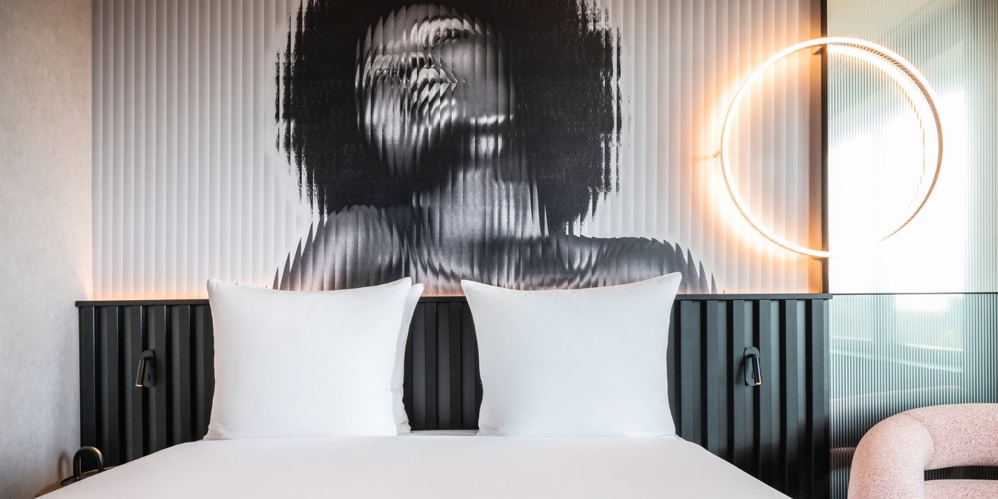 A double bed with white sheets in front of an artwork on the wall