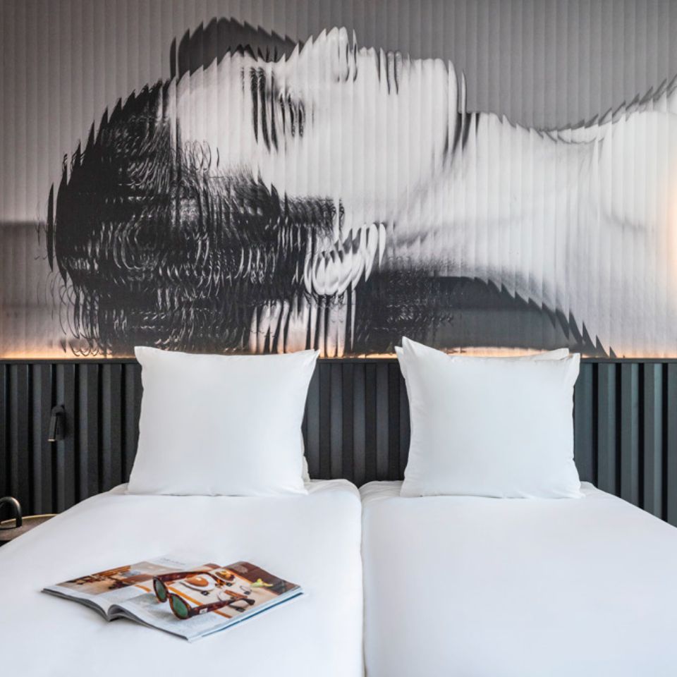 A double bed with white linens, on the wall is a black and white artpiece of a woman