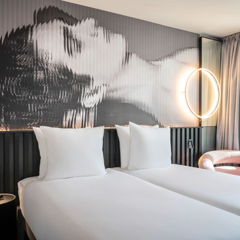 Two single beds with white linens, on the wall is a black and white artpiece of a woman