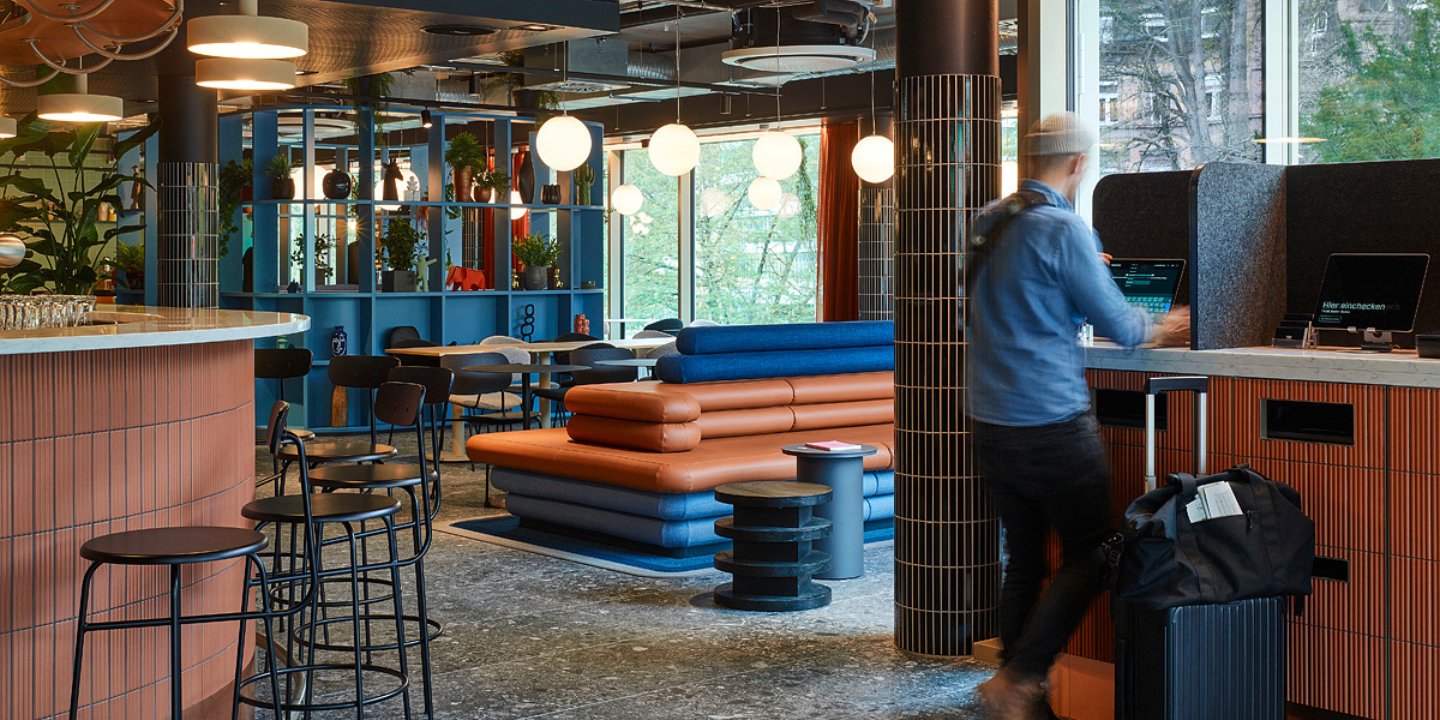 A vibrant workspace featuring colorful seating, plants, and soft lighting, with a person working at a sleek desk.