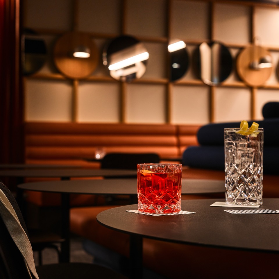 Two stylish cocktails on dark tables in a chic lounge, featuring a red drink and a clear one with lemon, set against a modern backdrop.