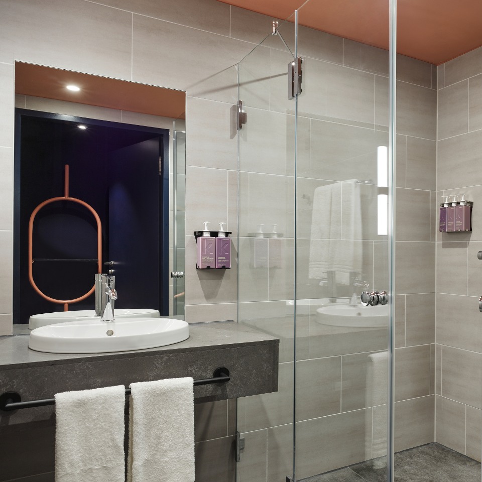 Modern bathroom featuring a glass shower, double sink with gray countertop, stylish towels, and wall-mounted toiletries.