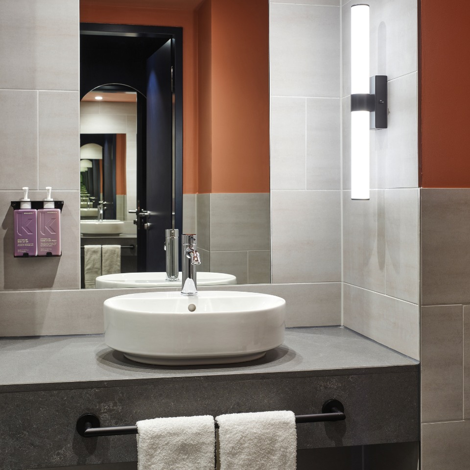 Modern bathroom featuring a round sink, gray countertop, wall-mounted light, and purple product dispensers with a stylish color scheme.