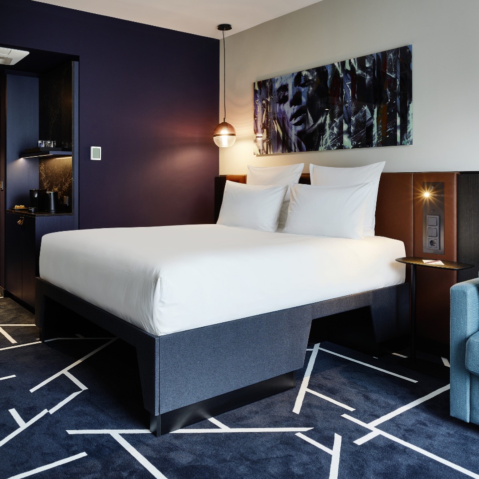 Hotel room featuring a large bed, stylish decor, and a cozy seating area with abstract artwork on the walls.