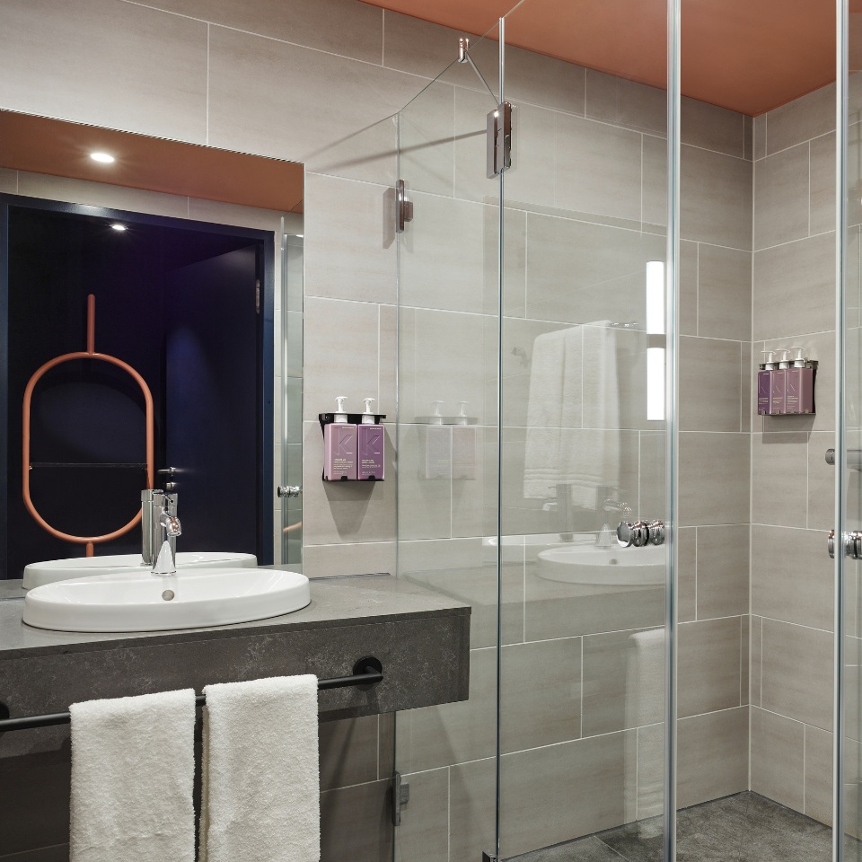 Modern bathroom featuring a glass shower, double sink with gray countertop, stylish towels, and wall-mounted toiletries.