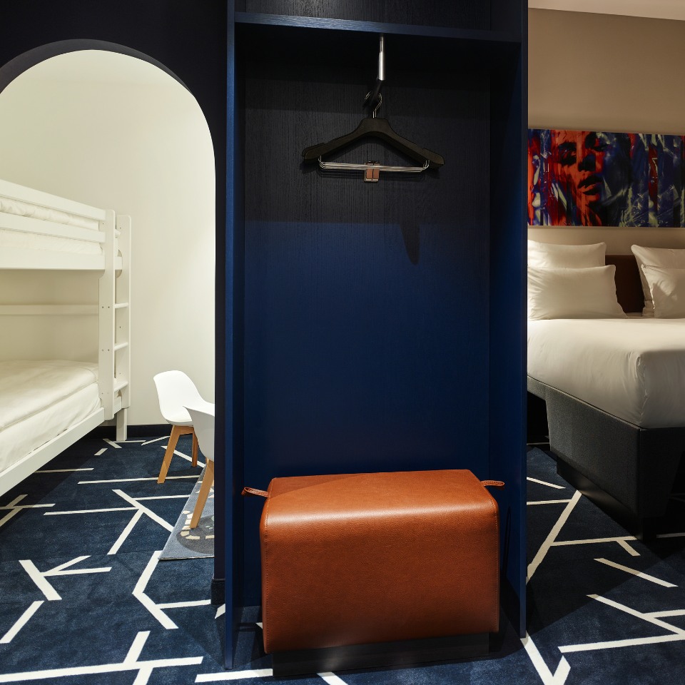 A modern hotel room featuring a bunk bed, a double bed, and a stylish blue closet with a hanger and chair accent.