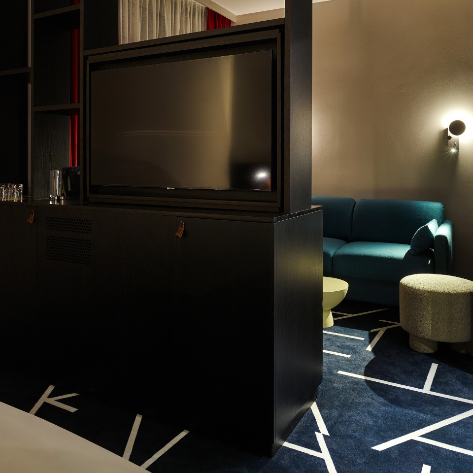 Modern hotel room showcasing a black entertainment unit with a television, blue sofa, round table, and stylish carpet.