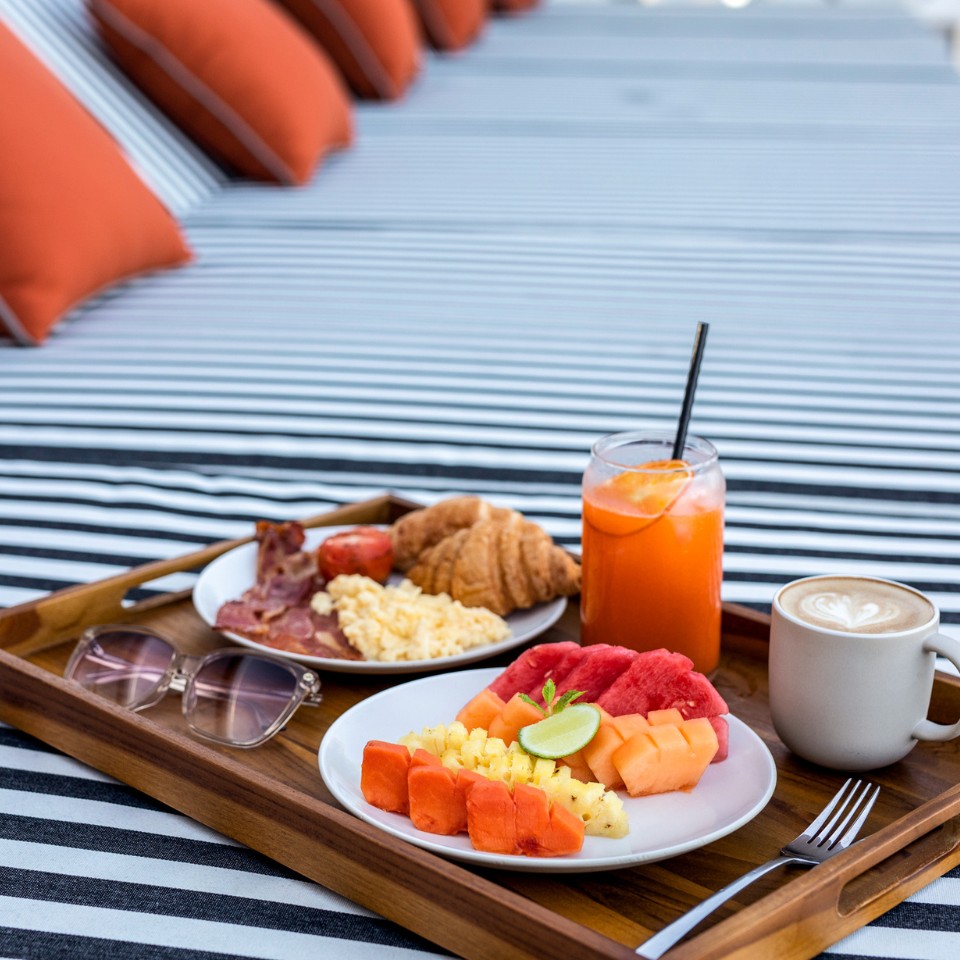 A serving tray with fresh fruit, juice, coffee and other breakfast dishes at a lounge sofa