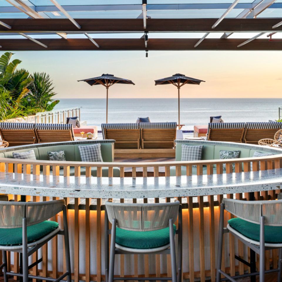 A round outdoor bar with bar chairs around it, overlooking the ocean