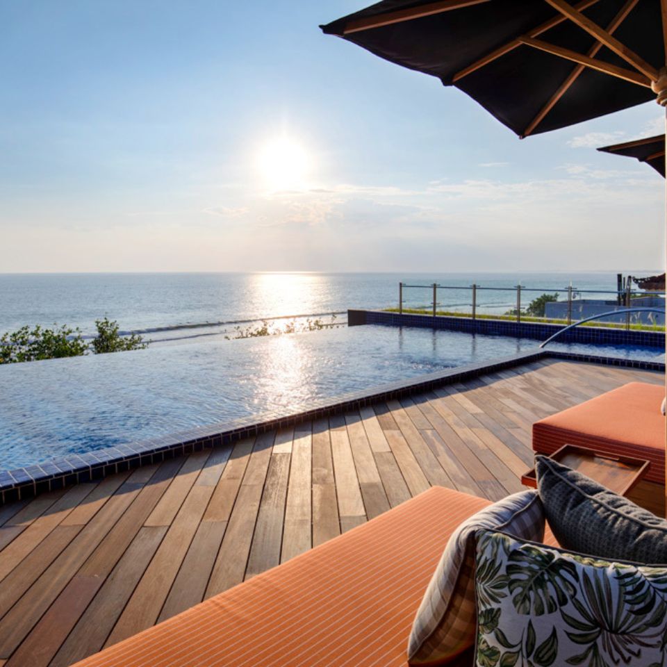 A rooftop pool and orange lounges with pillows on it