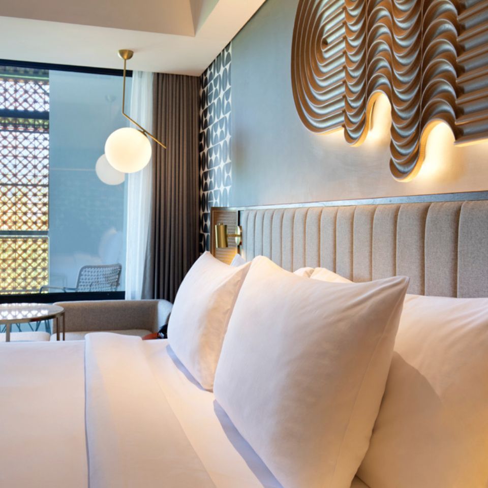 A double bed with white linen, plush pillows and a wooden art element on the wall above the headboard