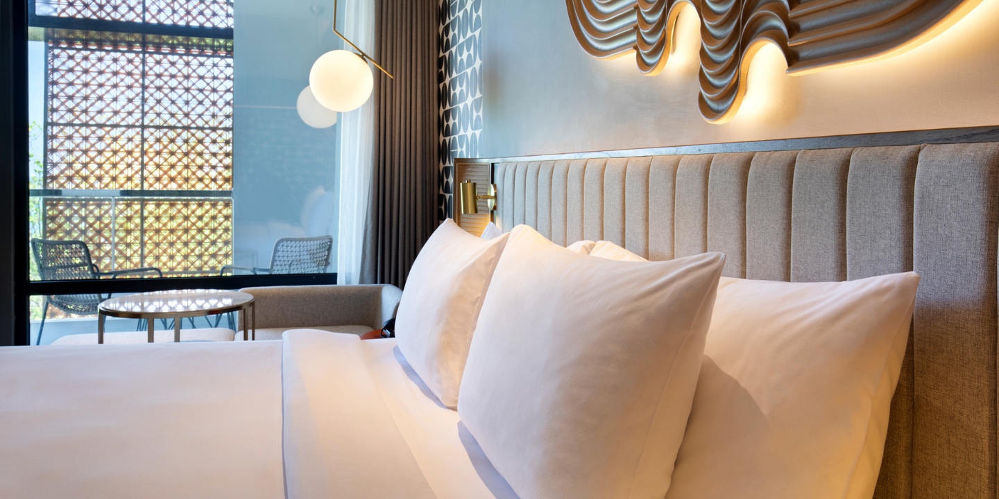 Double bed with white linens and a balcony in the background