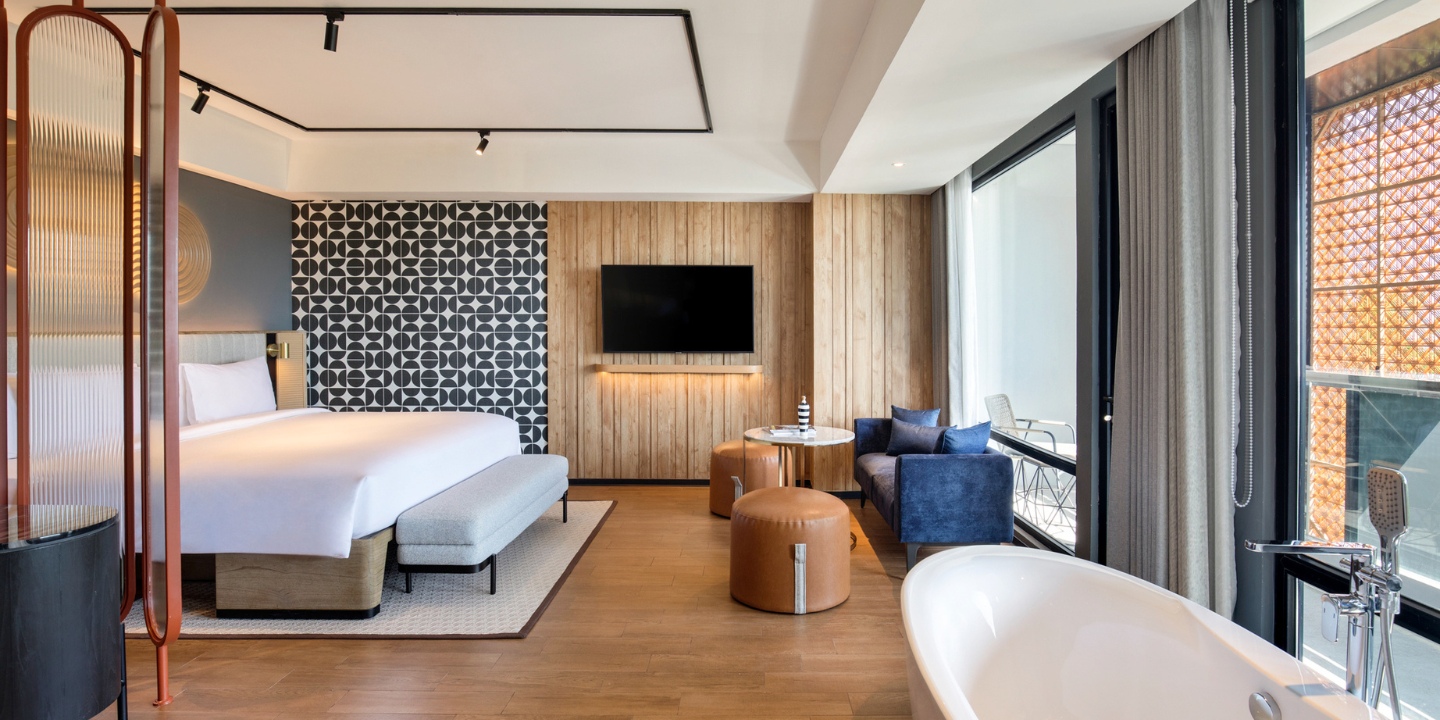 Suite at TRIBE Bali Kuta Beach with a double bed, a couch and table and a bathtub