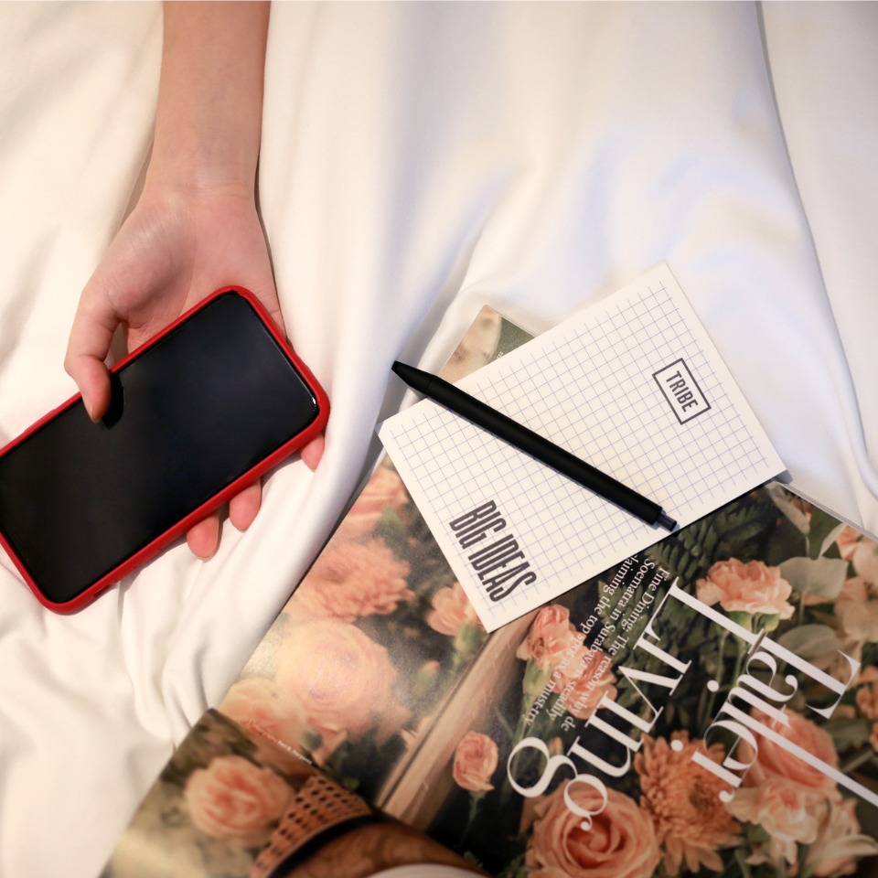 A hand holding a phone next to a notepad and a magazine