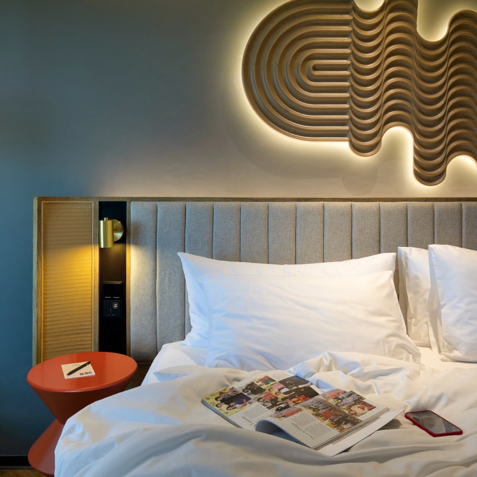 A double bed with an orange nightstand, a magazine is played open on the bed