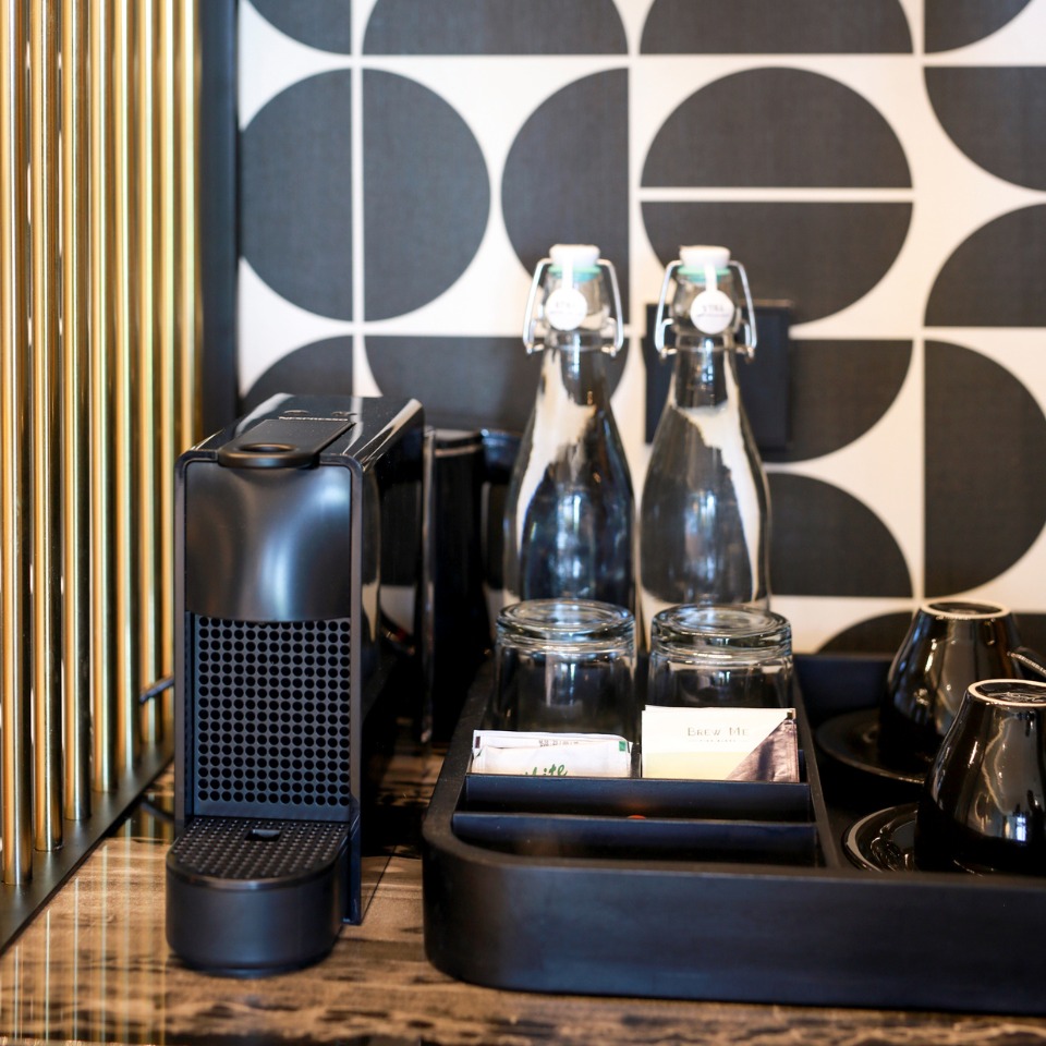 A coffee machine and water bottles with glasses in a tray
