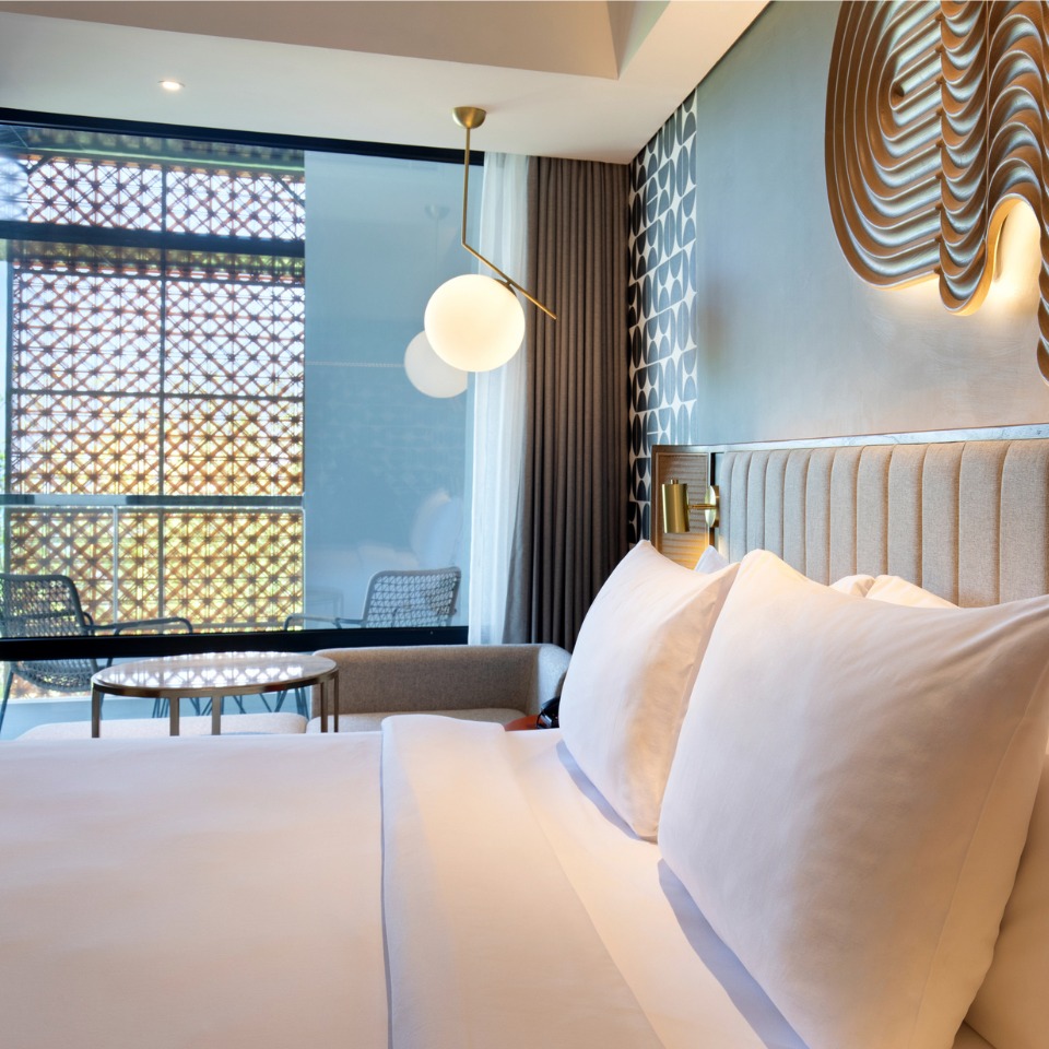 Double bed with white linens and a balcony in the background