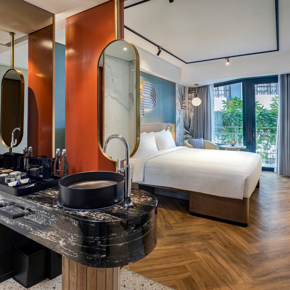 Sink with marble decor and golden mirrors in a hotelroom. The double bed and floor length windows are visible in the background
