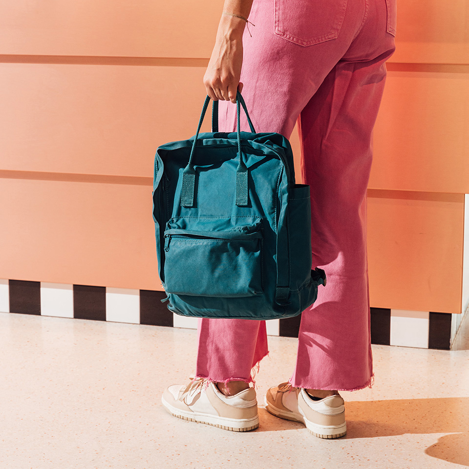 A person with pink pants holding a sporty backpack next to hear.