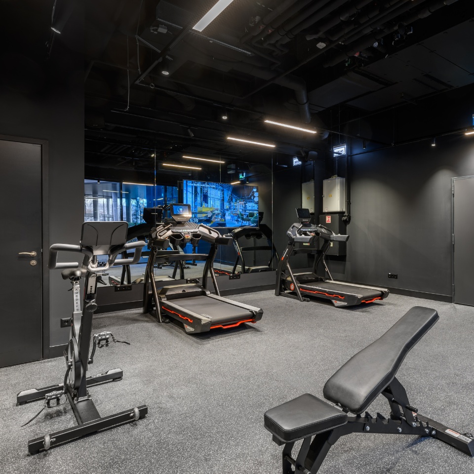 Gym interior featuring treadmills, a stationary bike, and a weight bench, all set against a sleek black backdrop.