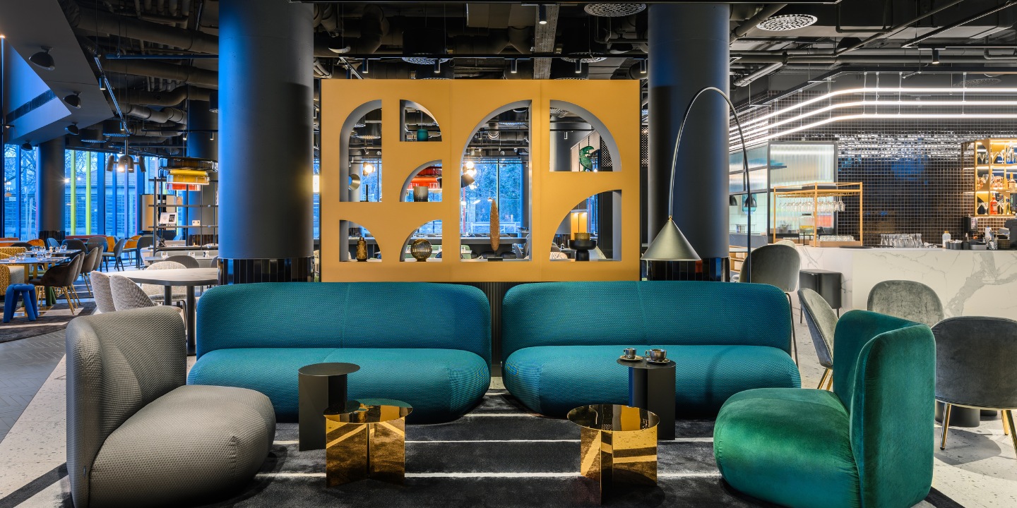 Lounge with teal and green sofas, gold tables, and vibrant decor; cozy ambiance enhanced by stylish lighting.