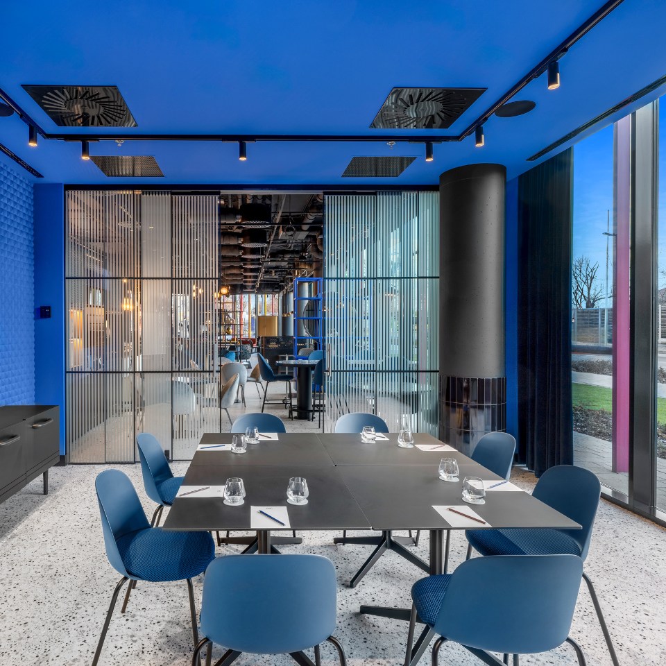 A meeting room with a black table, blue chairs, and vibrant blue walls, featuring glass partitions and large windows.