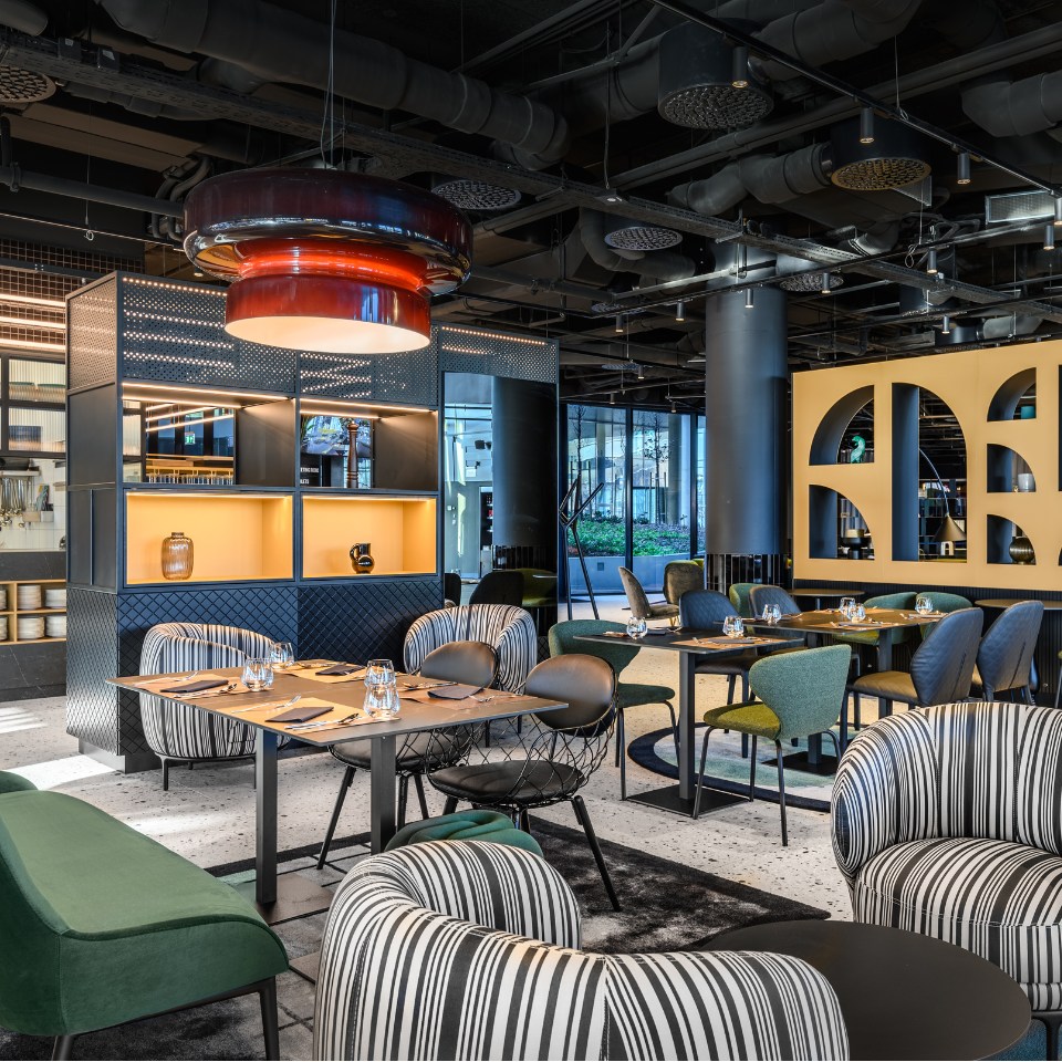 Modern restaurant interior with diverse seating, bold lighting, and stylish decor, featuring green and striped chairs, creating a vibrant atmosphere.