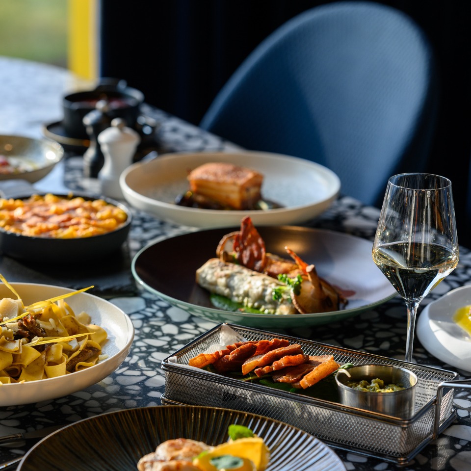 A beautifully arranged table featuring delicious dishes, including pasta, savory rolls, and a glass of white wine.