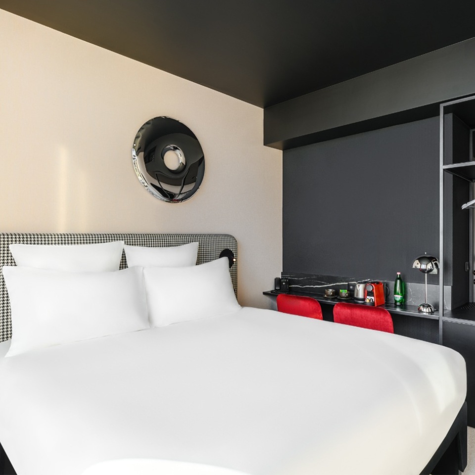 Hotel room featuring a large white bed, stylish black and red accents, and a small kitchenette area.