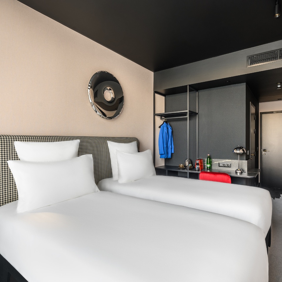 Hotel room featuring two twin beds, a stylish wall mirror, and a desk with a sleek design in neutral tones and pops of color.