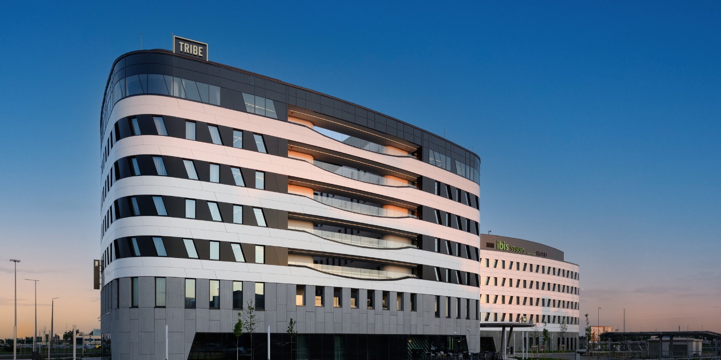 Modern curved building with alternating black and white bands under a clear blue sky. Nearby, another angular structure in white is visible.