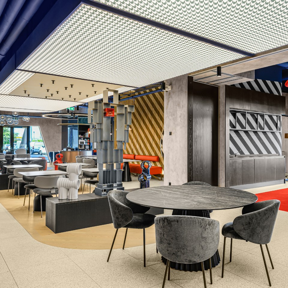 Modern dining area with plush chairs, unique decor, and a colorful robot sculpture, featuring vibrant design elements and open space.