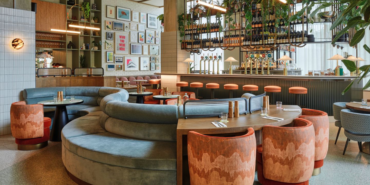 A large round couch and tables with chairs, in the background is a bar