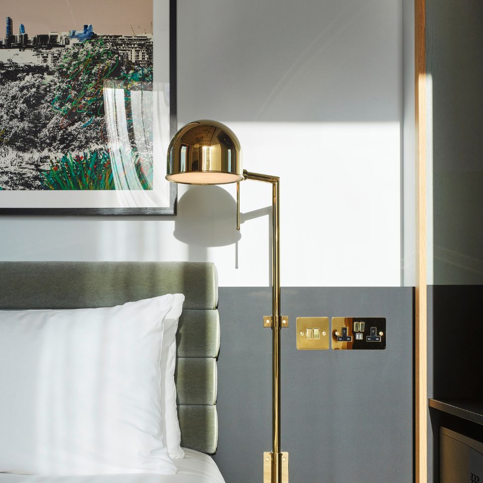 A hotel bed with a green headboard and a golden lamp