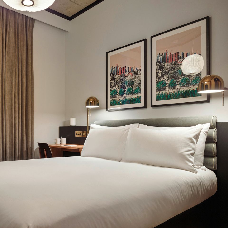 A double bed with white linens and framed pictures above it