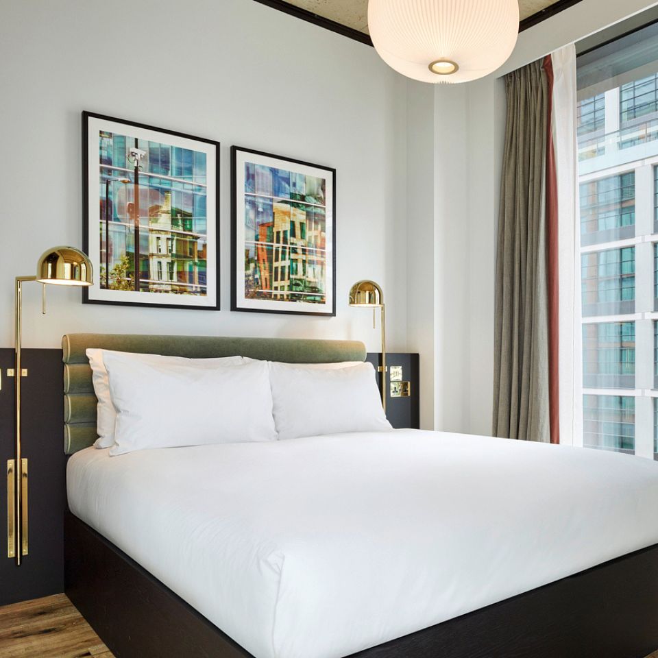 A double bed with white linens and framed pictures above it