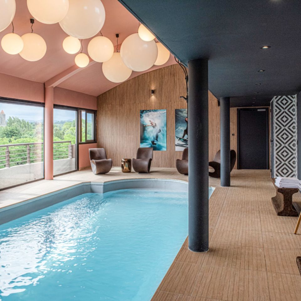 Small indoor pool with four reclining chairs and a view of a medieval city out of a window