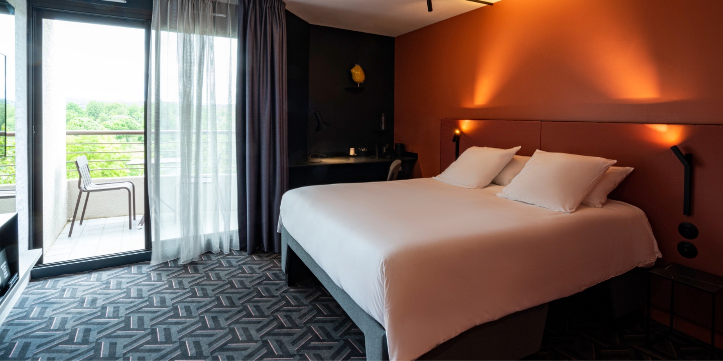 Full view of hotel room with double bed and sliding glass door leading to a balcony