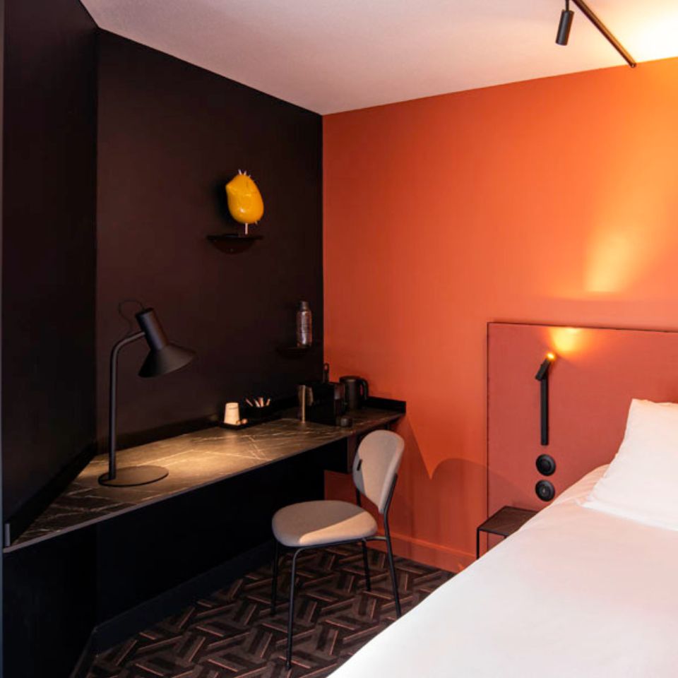 A black desk with a chair in a hotel room. The walls are black and orange.