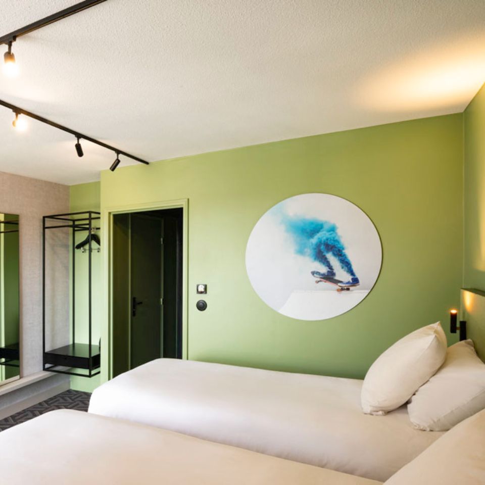 Hotel room with two single beds, clothes rack and mounted artwork depicting a skateboard