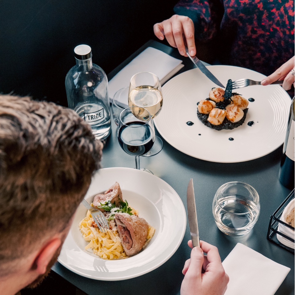 Two people eating lunch at a restaurant, there is wine and water on the table