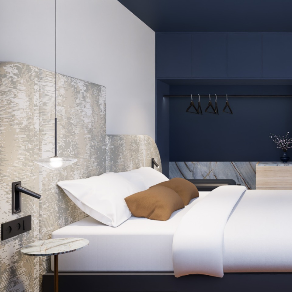 A hotel room featuring a double bed and a wardrobe, with a muted dark blue colour scheme.