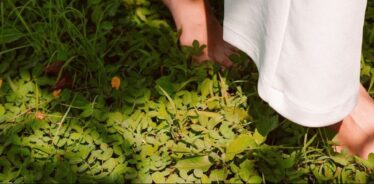 a person's feet walking through green pasture with white pants on