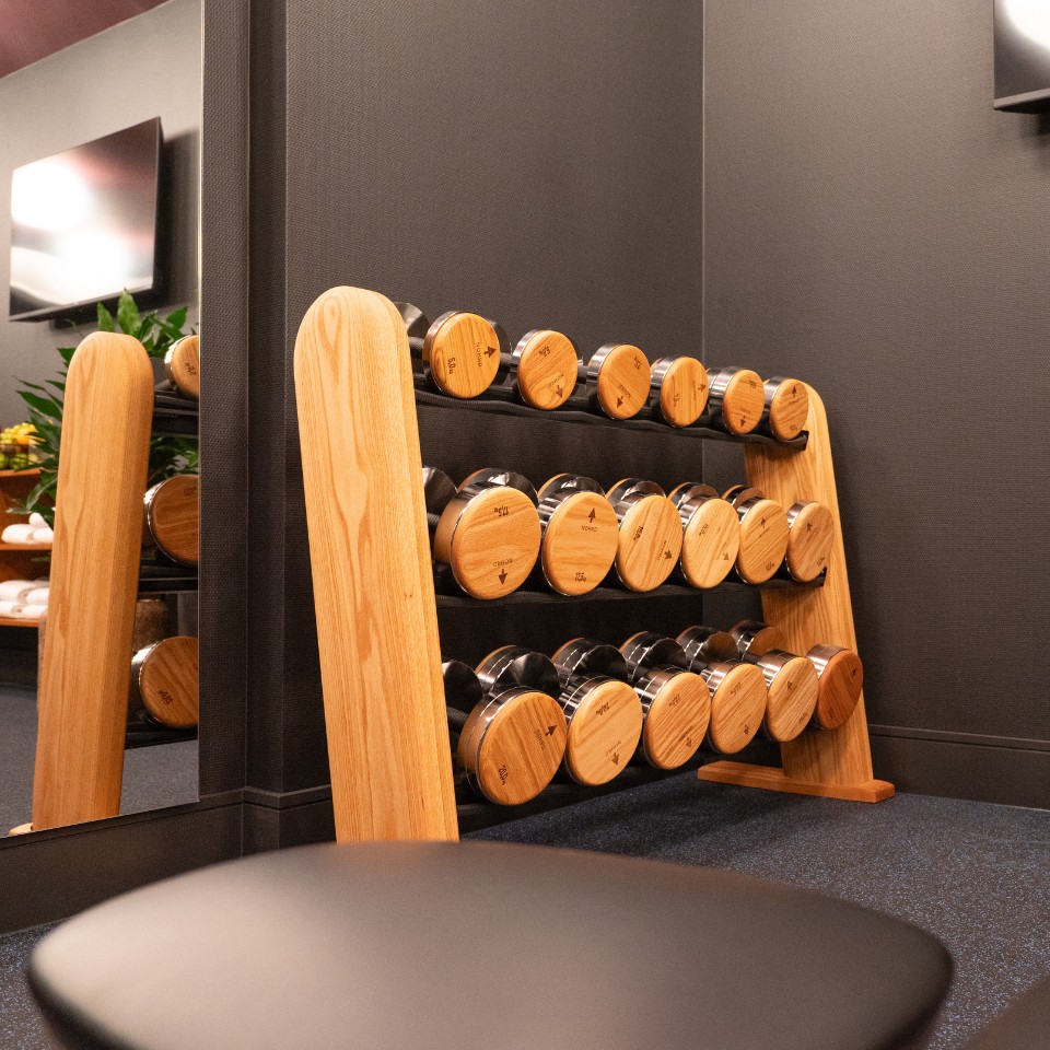 A wooden dumbbell rack featuring metal weights with wooden tops, set against a dark wall in a modern gym.