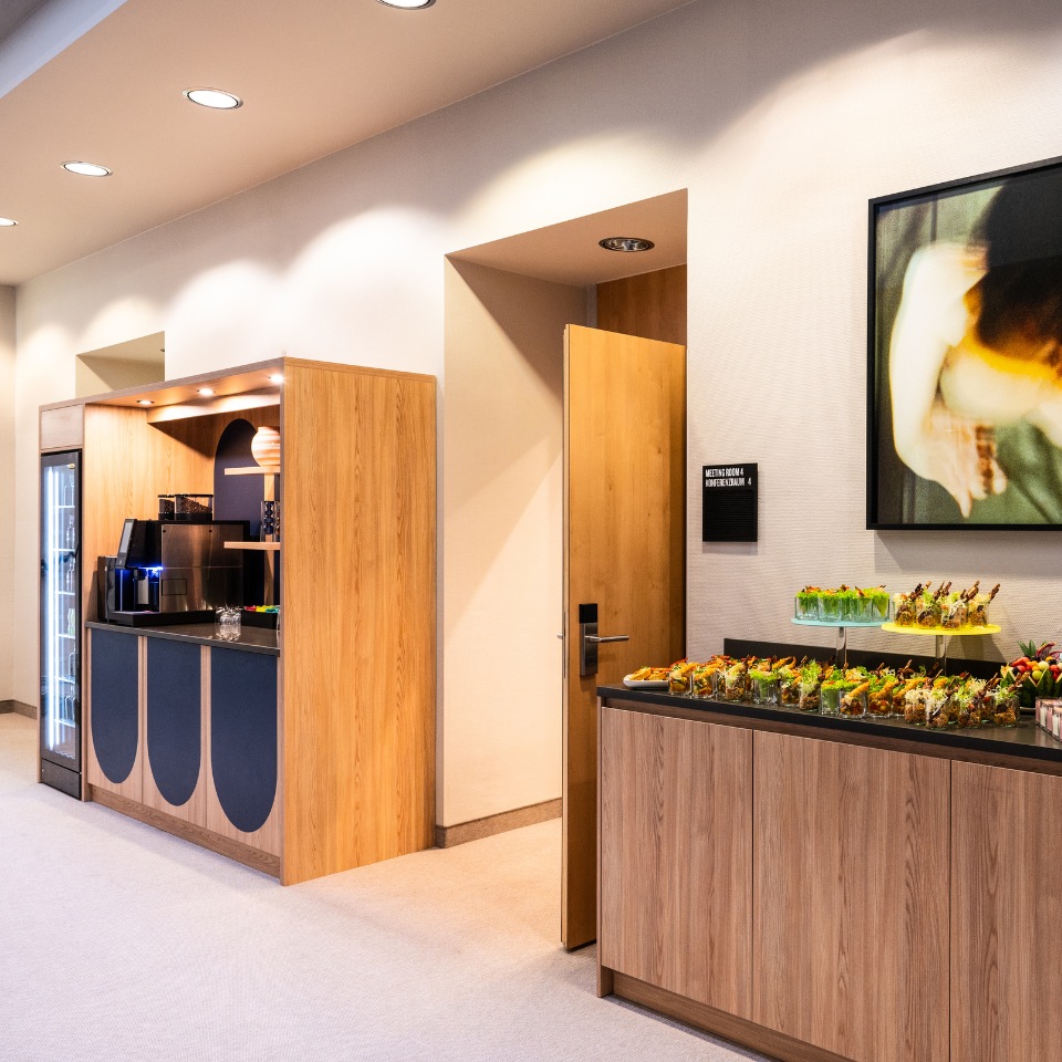 Inviting lounge area featuring a wooden snack bar, refreshments, art, and an open door to a meeting room.