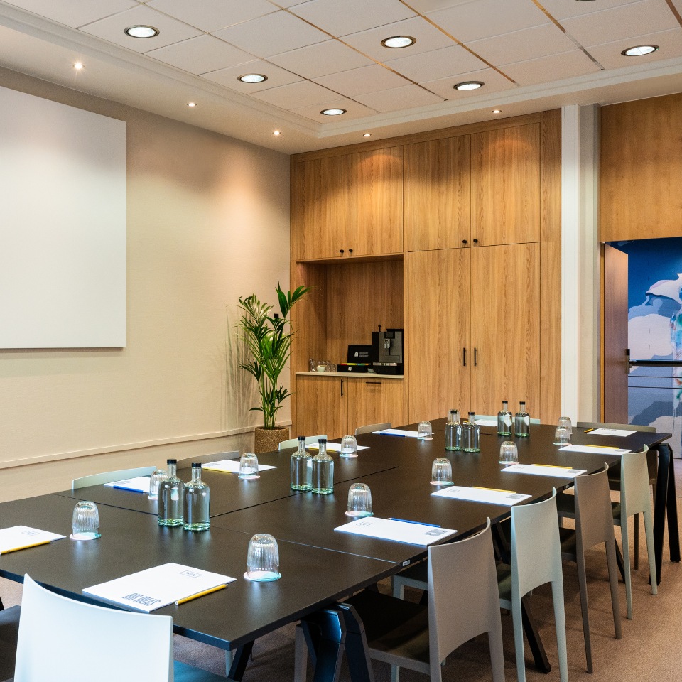 Modern meeting room featuring a long black table, glass water bottles, and wooden cabinetry, with a small plant in the corner.