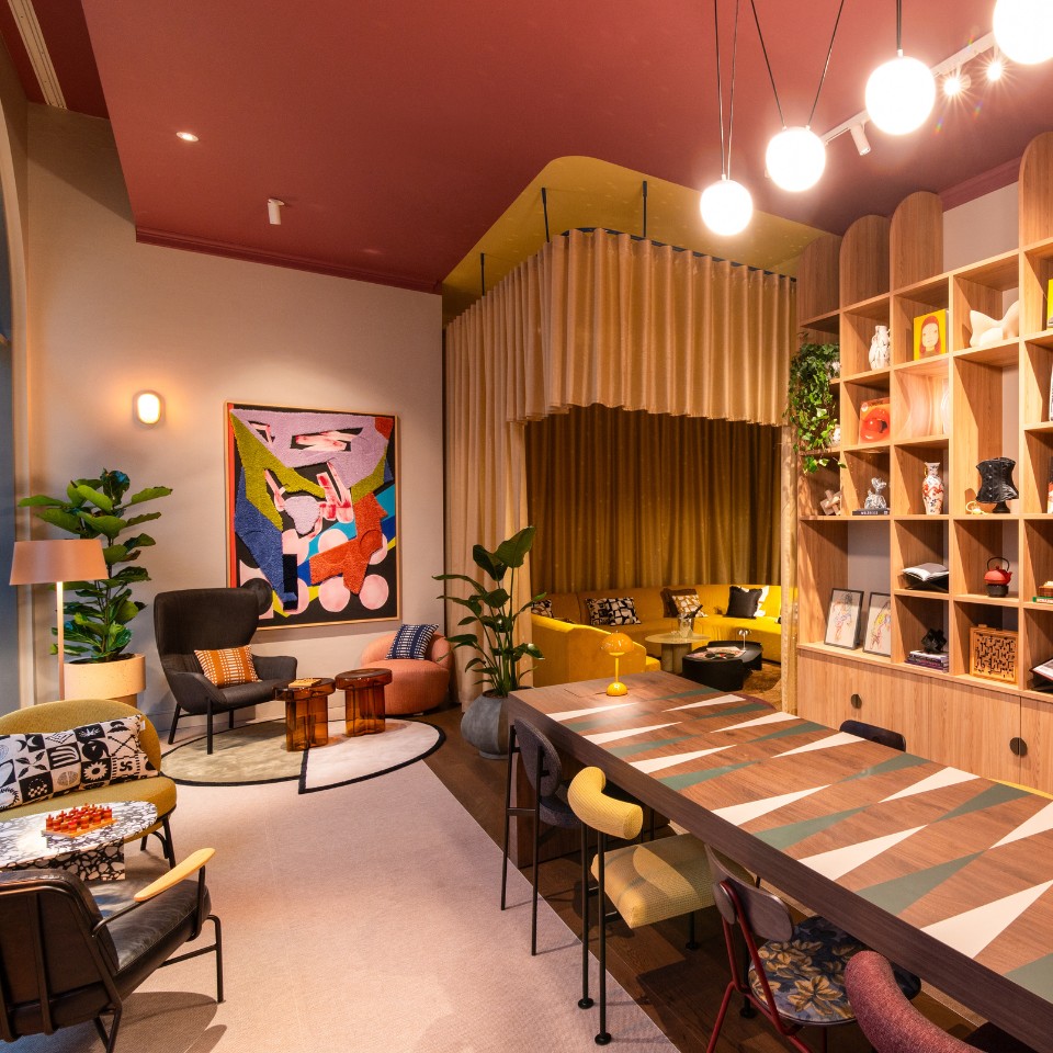 Stylish lounge with colorful seating, a modern art piece, greenery, and a sleek dining table, creating a cozy atmosphere.