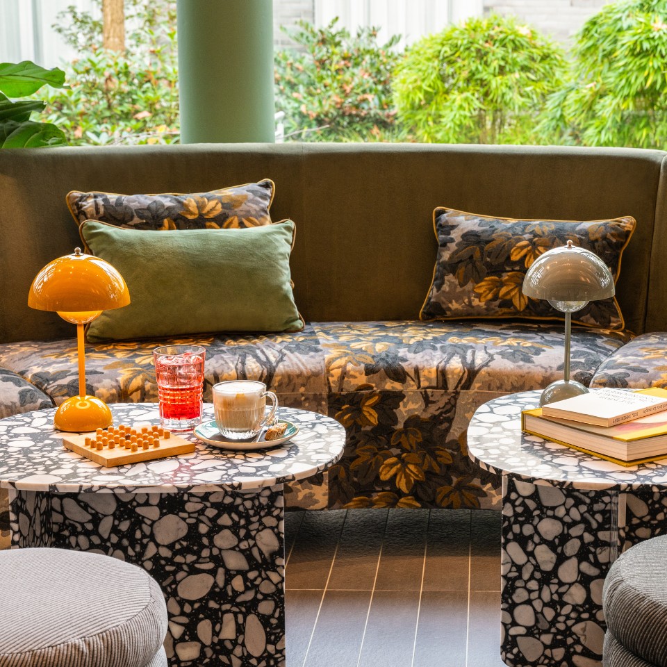 A lounge area with a floral-patterned sofa, stylish side tables with drinks, and decorative lamps, surrounded by greenery.