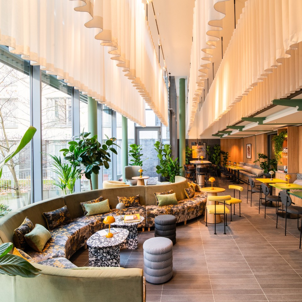 Modern lounge featuring a curved sofa, vibrant decor, greenery, and bright lighting, creating a cozy, inviting atmosphere.