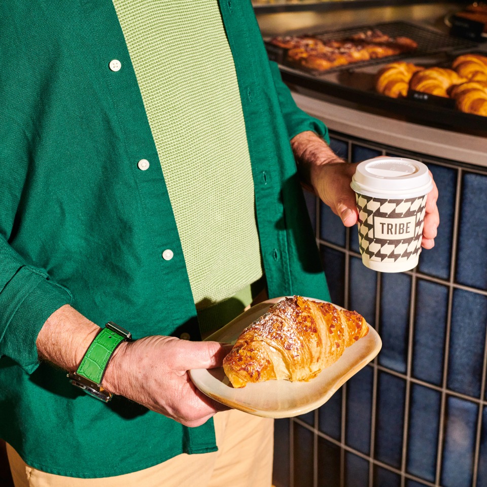 A person holding a croissant and a to-go coffee cup